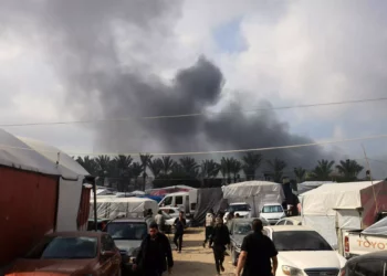 Varias personas caminan dentro de un refugio temporal para desplazados mientras se levanta humo durante un ataque israelí en Khan Yunis, en el sur de la Franja de Gaza, el 1 de diciembre de 2023. (Foto de Mahmud HAMS / AFP)