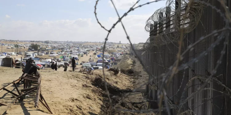 Palestinos desplazados por la ofensiva aérea y terrestre israelí sobre la Franja de Gaza sentados junto a la valla fronteriza con Egipto en Rafah, el miércoles 24 de enero de 2024. (AP/Hatem Ali)