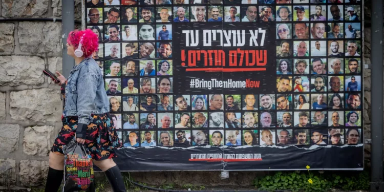Varias personas caminan junto a fotografías de civiles retenidos como rehenes por terroristas de Hamás en Gaza, en Jerusalén, el 12 de febrero de 2024. Chaim Goldberg/Flash90)