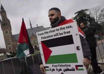 Un manifestante propalestino y antiisraelí sostiene un cartel frente a la Corte Internacional de Justicia, en la parte trasera, en La Haya, Países Bajos, el 21 de febrero de 2024. (AP Foto/ Peter Dejong)