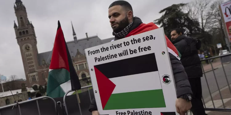 Un manifestante propalestino y antiisraelí sostiene un cartel frente a la Corte Internacional de Justicia, en la parte trasera, en La Haya, Países Bajos, el 21 de febrero de 2024. (AP Foto/ Peter Dejong)