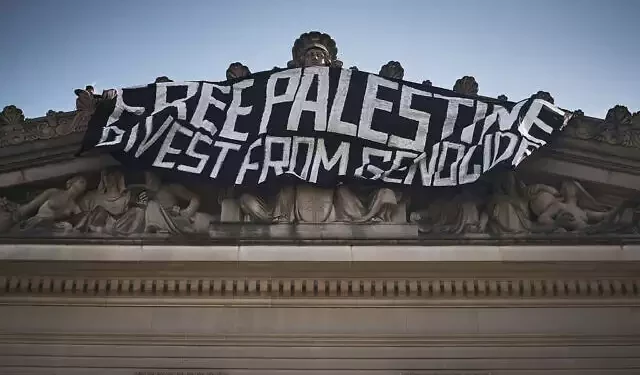 A pro-Palestinian demonstrator, upper left, hangs a flag on top of the Brooklyn Museum while occupying the building to protest Israel over its war with Hamás in Gaza, May 31, 2024, in New York. (AP Photo/Andres Kudacki)