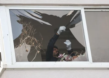 Un policía recoge metralla de vidrio de la ventana de un edificio dañado por un ataque con drones en Tel Aviv el 19 de julio de 2024 (GIL COHEN-MAGEN / AFP)