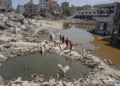 Palestinos caminan sobre los escombros de edificios destruidos, entre dos charcos de agua estancada en Jan Yunis, en el sur de la Franja de Gaza, el 19 de julio de 2024 (Bashar TALEB / AFP)