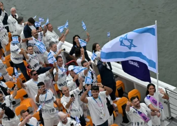 La delegación de Israel con los abanderados de Israel, Peter Paltchik (2.° a la derecha) y Andrea Murez (2.° a la derecha), navega en un barco durante la ceremonia de apertura de los Juegos Olímpicos de París 2024 en París el 26 de julio de 2024. (Damien Meyer/AFP)