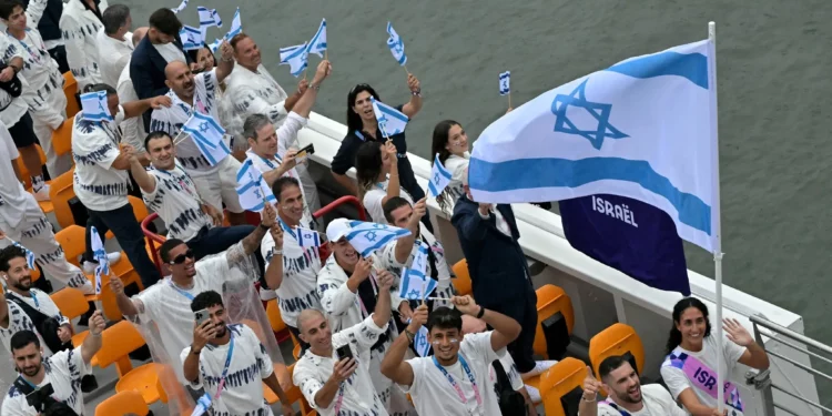 La delegación de Israel con los abanderados de Israel, Peter Paltchik (2.° a la derecha) y Andrea Murez (2.° a la derecha), navega en un barco durante la ceremonia de apertura de los Juegos Olímpicos de París 2024 en París el 26 de julio de 2024. (Damien Meyer/AFP)