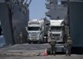 Soldados del ejército de Estados Unidos hacen un gesto mientras camiones cargados con ayuda humanitaria llegan al muelle flotante Trident, construido por Estados Unidos, antes de llegar a la playa en la costa de la Franja de Gaza, el 25 de junio de 2024. (Foto AP/Leo Correa)