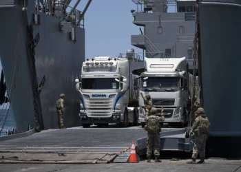 Soldados del ejército de Estados Unidos hacen un gesto mientras camiones cargados con ayuda humanitaria llegan al muelle flotante Trident, construido por Estados Unidos, antes de llegar a la playa en la costa de la Franja de Gaza, el 25 de junio de 2024. (Foto AP/Leo Correa)