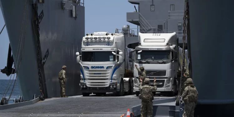 Soldados del ejército de Estados Unidos hacen un gesto mientras camiones cargados con ayuda humanitaria llegan al muelle flotante Trident, construido por Estados Unidos, antes de llegar a la playa en la costa de la Franja de Gaza, el 25 de junio de 2024. (Foto AP/Leo Correa)