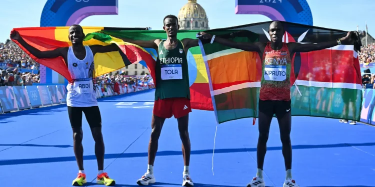 El etíope ganador Tamirat Tola (centro), el belga Bashir Abdi (izq.), segundo clasificado, y el keniano Benson Kipruto, tercero, celebran después del maratón masculino de la prueba de atletismo de los Juegos Olímpicos de París 2024 en Inválidos, en París, el 10 de agosto de 2024. (Andrej Isakovic/AFP)