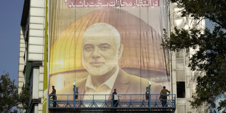 Trabajadores iraníes instalan una enorme pancarta en una pared que muestra un retrato del líder del grupo terrorista Hamás, Ismail Haniyeh, y el santuario islámico Cúpula de la Roca en la cima del Monte del Templo en Jerusalén con un cartel que dice en farsi y hebreo: “Esperen un castigo severo”, en la Plaza Palestina en Teherán, Irán, el 31 de julio de 2024. Haniyeh fue asesinado en la ciudad horas antes. (Foto AP/Vahid Salemi)