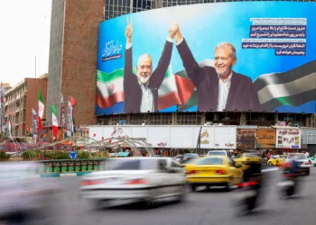 Los vehículos pasan junto a una enorme valla publicitaria que representa al presidente iraní Masoud Pezeshkian (derecha) y al líder palestino asesinado de Hamás, Ismail Haniyeh, en la plaza Valiasr de Teherán el 12 de agosto de 2024. (Atta Kenare/ AFP)