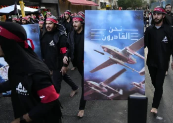Miembros del Hezbolá, respaldado por Irán, caminan descalzos mientras llevan un cartel que muestra drones del Hezbolá que dice, en árabe, “Estamos llegando”, durante el día sagrado de Ashura en el suburbio sur de Beirut, Líbano, el 9 de agosto de 2022. (Foto AP/Hussein Malla, Archivo)