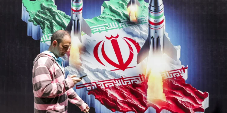 Un hombre pasa junto a una pancarta que muestra el lanzamiento de misiles desde una representación del mapa de Irán coloreado con la bandera iraní en el centro de Teherán, el 15 de abril de 2024. (ATTA KENARE / AFP)