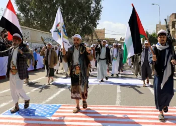 Hombres yemeníes armados pisan una bandera estadounidense e israelí pintadas en el asfalto en la capital gobernada por los hutíes, Saná, durante una marcha en apoyo a los palestinos, el 29 de febrero de 2024. (MOHAMMED HUWAIS / AFP)