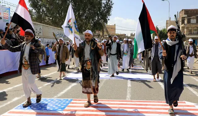 Hombres yemeníes armados pisan una bandera estadounidense e israelí pintadas en el asfalto en la capital gobernada por los hutíes, Saná, durante una marcha en apoyo a los palestinos, el 29 de febrero de 2024. (MOHAMMED HUWAIS / AFP)