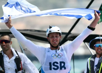 El israelí Tom Reuveny celebra con la bandera nacional después de ganar la medalla de oro en la final masculina de windsurf IQFoil en la competición de vela de los Juegos Olímpicos de París 2024, en la Marina Roucas-Blanc en Marsella el 3 de agosto de 2024. (Christophe SIMON / AFP)