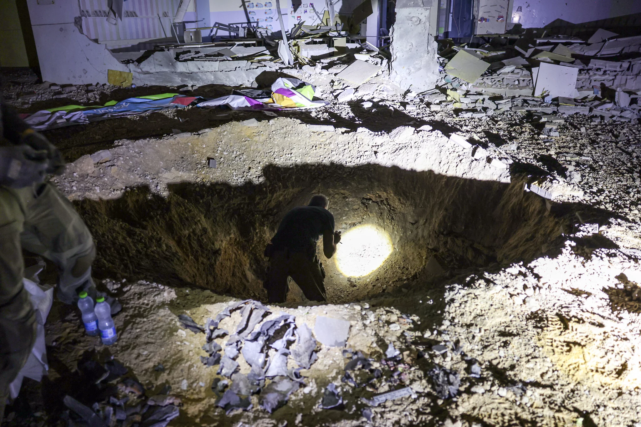 Miembros del Comando del Frente Interno de Israel y fuerzas policiales inspeccionan un cráter dejado por un proyectil que explotó en un edificio escolar gravemente dañado en la ciudad de Gedera, en el sur de Israel, el 1 de octubre de 2024, después de que Irán lanzara una andanada de misiles contra Israel (Menahem KAHANA / AFP)