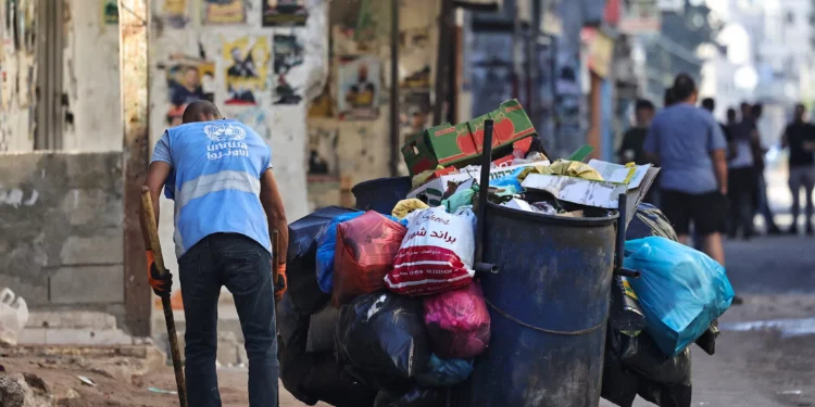 Un hombre que viste una chaqueta con el logo de UNRWA recoge basura en una calle del campamento de Balata, al este de Nablús, en el norte de Judea y Samaria, el 15 de agosto de 2024. (Zain Jaafar/AFP)