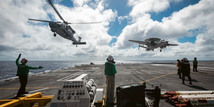Un MH-60S Sea Hawk y un E-2D Hawkeye, asignados a los “Grey Hawks” del Escuadrón de Comando y Control Aerotransportado (VAW) 120, se aproximan a la cubierta de vuelo del USS Gerald R. Ford (CVN-78). (Fotografía de la Marina de los EE. UU. realizada por el especialista en comunicación de masas de segunda clase Maxwell Orlosky)