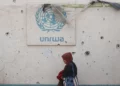 Una mujer palestina pasa junto a un muro dañado con el logotipo de la UNRWA en un campamento para desplazados internos en Rafah, en el sur de la Franja de Gaza, el 28 de mayo de 2024. (Eyad Baba/AFP)