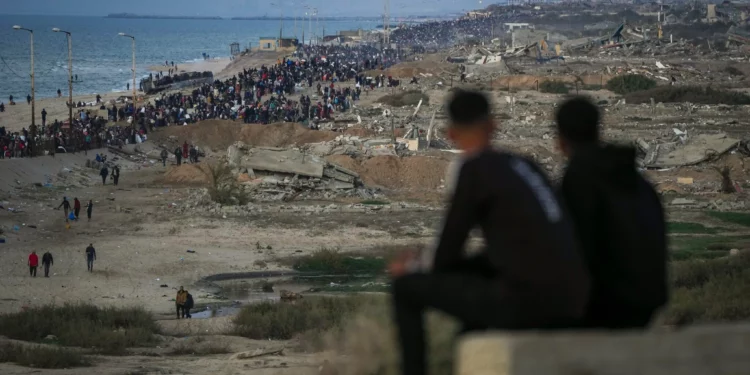 Dos niños observan a una multitud de palestinos que regresan al norte de Gaza, en medio de edificios destruidos, el 27 de enero de 2025. (AP/Abdel Kareem Hana)