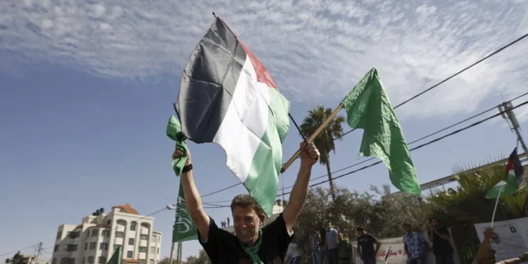 El terrorista de Hamás Nael Barghouti ondea una bandera islámica verde y una bandera palestina ante la multitud después de llegar a la ciudad de Ramallah, tras ser liberado como parte de un intercambio por Gilad Shalit, un soldado israelí retenido por Hamás, el 18 de octubre de 2011. (AP/Majdi Mohammed)