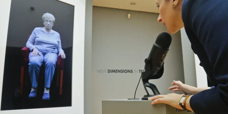 Ilustrativo: Josephine Mairzadeh utiliza un micrófono para plantear una pregunta a una presentación virtual de la sobreviviente del Holocausto Eva Schloss, que aparece en una instalación interactiva testimonial llamada “Nuevas dimensiones en el testimonio” en el Museo del Patrimonio Judío, en Nueva York, el 15 de septiembre de 2017. (Foto AP/Bebeto Matthews)