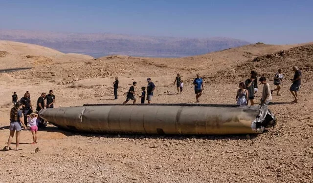 Israelíes observan los restos de un misil iraní, en el desierto de Negev, cerca de Arad, el 3 de octubre de 2024. (MENAHEM KAHANA / AFP)