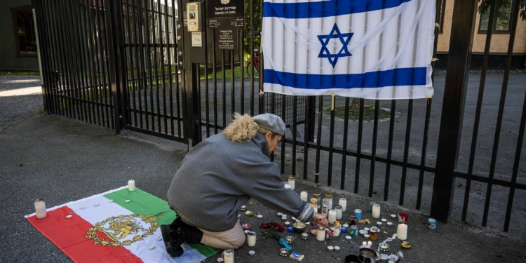 Una mujer enciende una vela para mostrar su apoyo frente a la embajada de Israel en Estocolmo, Suecia, el 9 de octubre de 2023, tras el ataque terrorista del 7 de octubre dirigido por Hamás contra Israel. En la valla hay una bandera israelí y en el suelo la histórica bandera de Irán. (Foto de Jonathan Nackstrand / AFP)