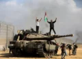 Palestinos ondean la bandera nacional y celebran junto a un tanque israelí destruido en la valla del sur de la Franja de Gaza, al este de Jan Yunis, el 7 de octubre de 2023. (Foto AP/Yousef Masoud)
