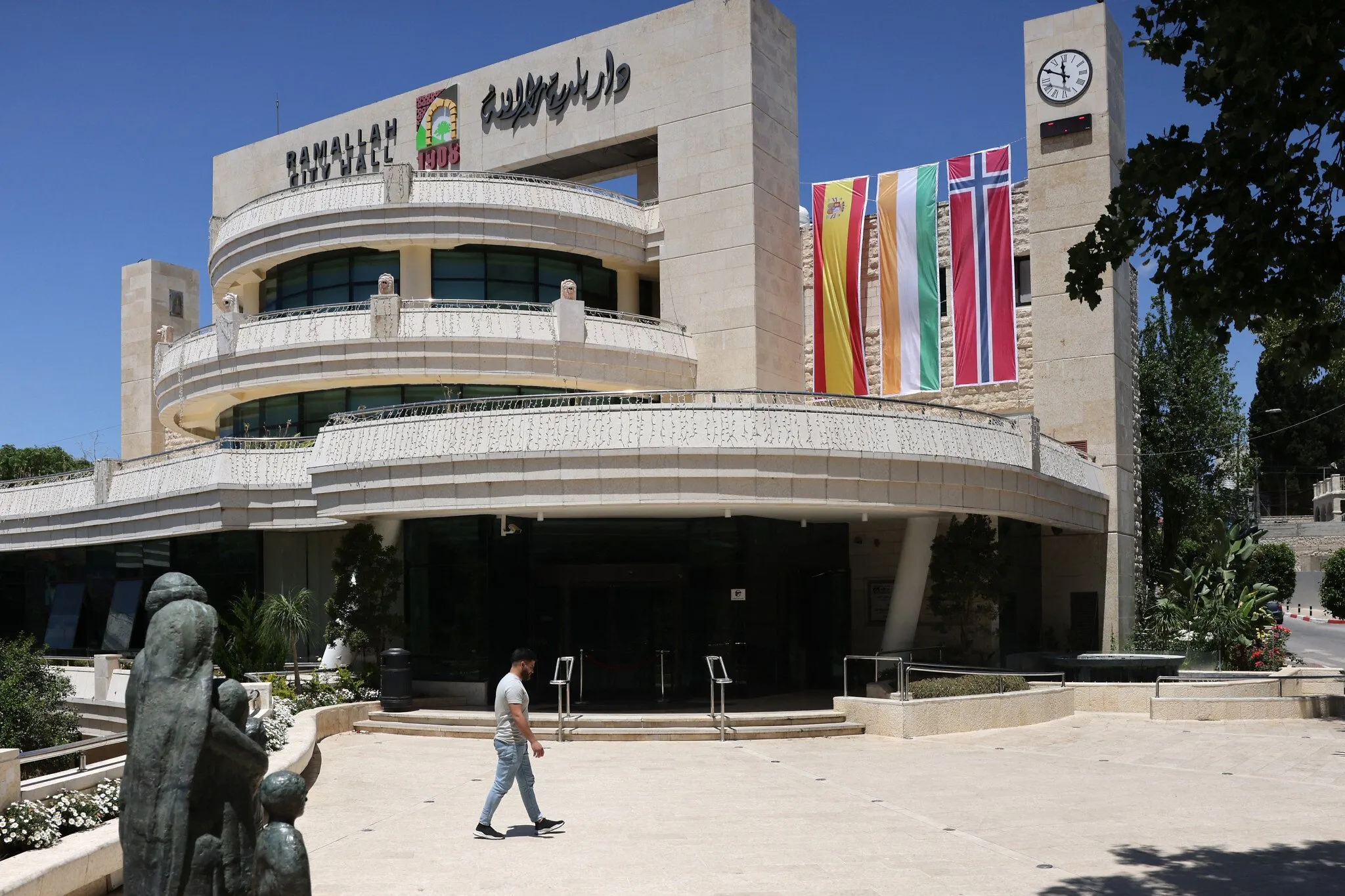 Un hombre camina fuera del edificio municipal en la ciudad de Ramala el 24 de mayo de 2024, adornado con banderas de España, Irlanda y Noruega después de que los países dijeran que reconocerían formalmente al Estado de Palestina. (Ahmad Gharabli/AFP)