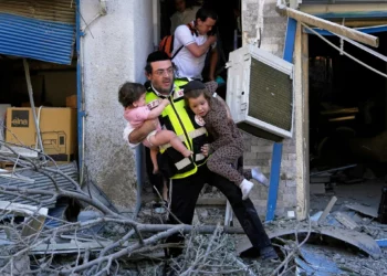 Un trabajador de rescate evacua a dos niños del lugar donde impactó un misil lanzado desde Irán en Haifa, Israel, el domingo 22 de junio de 2025. (AP Foto/Baz Ratner)