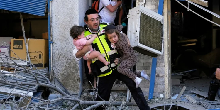 Un trabajador de rescate evacua a dos niños del lugar donde impactó un misil lanzado desde Irán en Haifa, Israel, el domingo 22 de junio de 2025. (AP Foto/Baz Ratner)