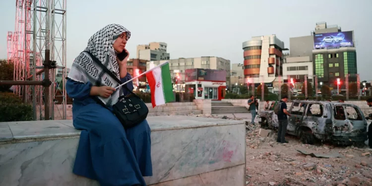 Una mujer iraní se sienta cerca de un vehículo destruido mientras observa y escucha una banda tradicional en la plaza Hafteh-tir en Teherán, el 23 de junio de 2025. (AFP)