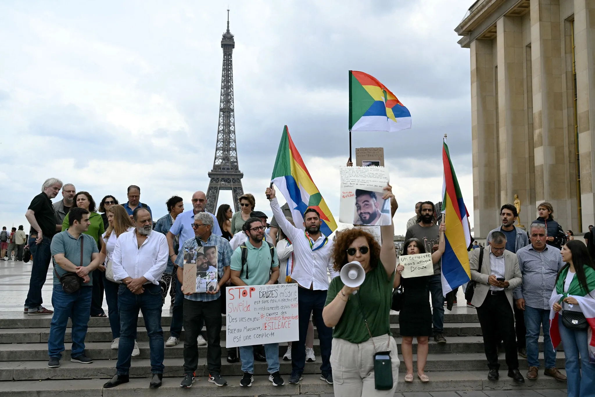 Los manifestantes sostienen carteles y banderas drusas con la estrella drusa durante una manifestación en apoyo de la comunidad drusa siria en la Place du Trocadero, con la Torre Eiffel al fondo en París el 19 de julio de 2025. (Bertrand GUAY / AFP)
