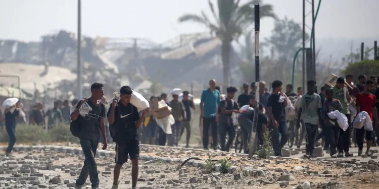Palestinos desplazados en el campo de refugiados de Nuseirat transportan paquetes de comida y otros artículos que consiguieron en un punto de distribución de ayuda de la GHF en el corredor de Netzarim, en el centro de la Franja de Gaza, el 26 de julio de 2025. (Eyad BABA / AFP)