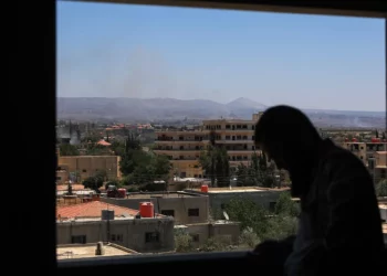 Un hombre se encuentra junto a una ventana mientras se elevan columnas de humo durante los ataques israelíes en las cercanías de la ciudad de Sweida, en el sur de Siria, el 16 de julio de 2025. (Bakr ALKASEM / AFP)