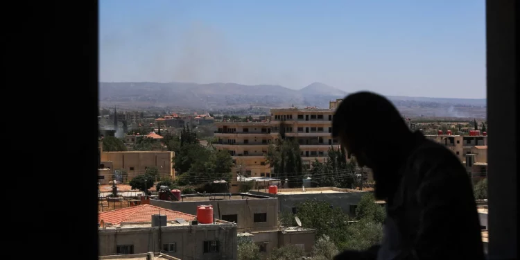 Un hombre se encuentra junto a una ventana mientras se elevan columnas de humo durante los ataques israelíes en las cercanías de la ciudad de Sweida, en el sur de Siria, el 16 de julio de 2025. (Bakr ALKASEM / AFP)