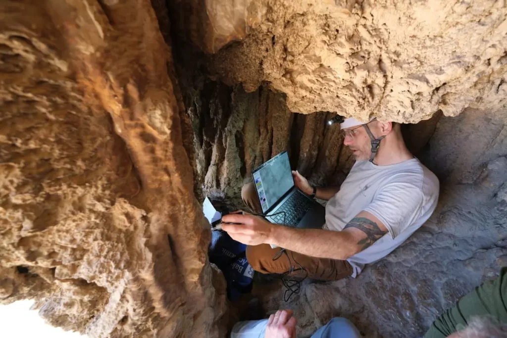 El Dr. Asaf Gayer, del Departamento de Estudios y Arqueología de la Tierra de Israel de la Universidad de Ariel, examina una cueva cerca del Parque Nacional Ein Gedi en la región del mar muerto, con una antigua inscripción aramea, posiblemente fechada en la revuelta de Bar Kojba, que se reveló por primera vez al público en agosto de 2025. (Asaf Gayer) 