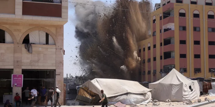 Gzatíes corren a resguardarse mientras el humo se eleva después de un ataque israelí contra un edificio en Yabalia, en el norte de la Franja de Gaza, el 20 de agosto de 2025. (BASHAR TALEB / AFP)