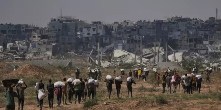 Gsazatíes llevan paquetes de ayuda humanitaria cerca de un centro de distribución de la Fundación Humanitaria de Gaza operado por la organización respaldada por Estados Unidos, en Netzarim, en el centro de la Franja de Gaza, el 4 de agosto de 2025. (AP Foto/Abdel Kareem Hana)