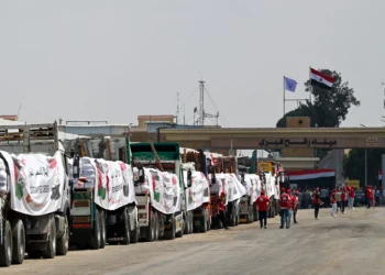 La gente pasa junto a camiones cargados con ayuda para Gaza que esperan en el cruce de Rafah del lado egipcio de la Franja, el 18 de agosto de 2025. (Khaled DESOUKI / AFP)