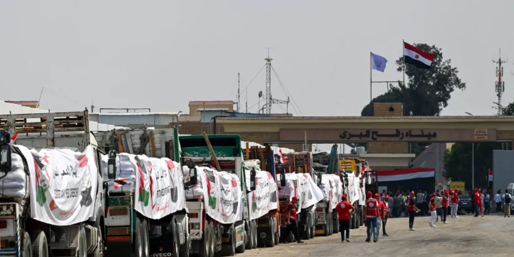 La gente pasa junto a camiones cargados con ayuda para Gaza que esperan en el cruce de Rafah del lado egipcio de la Franja, el 18 de agosto de 2025. (Khaled DESOUKI / AFP)
