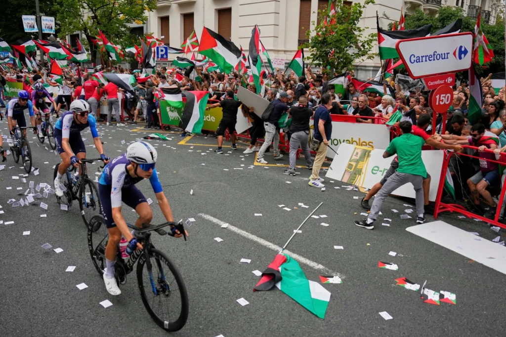 Ciclistas del equipo Israel Premier Tech compiten mientras personas con banderas palestinas intentan interrumpir la 11ª etapa de la Vuelta Ciclista a España, en Bilbao, España, el 3 de septiembre de 2025. (AP Foto/Miguel Oses) 