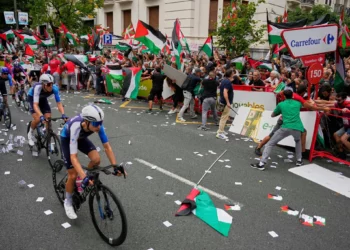 Ciclistas del equipo Israel Premier Tech compiten mientras personas con banderas palestinas intentan interrumpir la 11ª etapa de la Vuelta Ciclista a España, en Bilbao, España, el 3 de septiembre de 2025. (AP Foto/Miguel Oses)