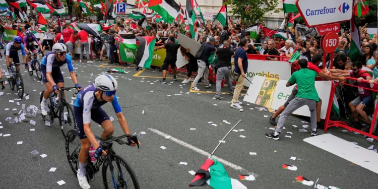 Ciclistas del equipo Israel Premier Tech compiten mientras personas con banderas palestinas intentan interrumpir la 11ª etapa de la Vuelta Ciclista a España, en Bilbao, España, el 3 de septiembre de 2025. (AP Foto/Miguel Oses)