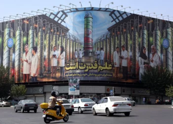 Los iraníes conducen junto a una valla publicitaria que muestra imágenes de científicos nucleares, centrifugadoras y una frase que dice en farsi: “La ciencia es el poder” en la plaza Enqelab de Teherán, el 29 de agosto de 2025 (AFP)