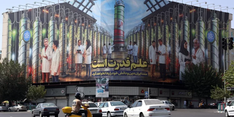 Los iraníes conducen junto a una valla publicitaria que muestra imágenes de científicos nucleares, centrifugadoras y una frase que dice en farsi: “La ciencia es el poder” en la plaza Enqelab de Teherán, el 29 de agosto de 2025 (AFP)