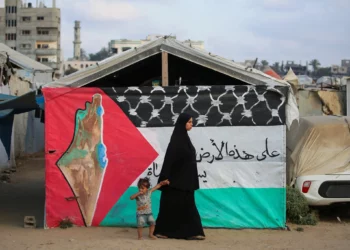 Una mujer palestina camina con un niño junto a una bandera palestina en el campamento de Bureij, en el centro de la Franja de Gaza, el 22 de septiembre de 2025. (Foto de Eyad BABA / AFP)